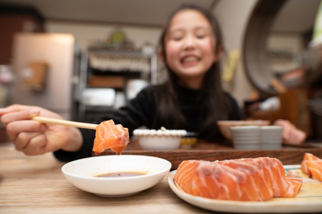 Young girl eating sushi, dipping it in soy sauce