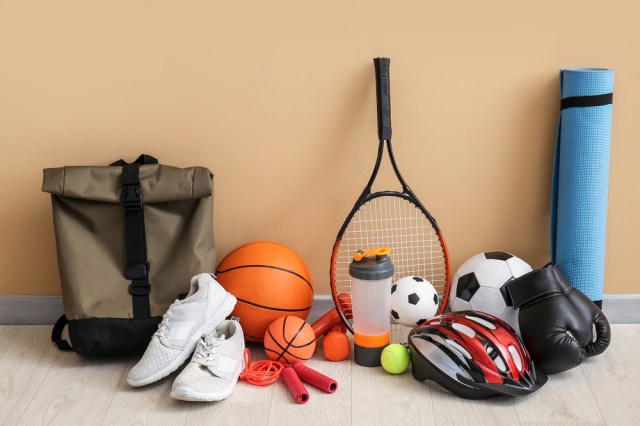 Sports equipment - tennis racket, shoes, bag, yoga mat, basketball, soccer ball, baseball glove, etc - against a plain beige wall