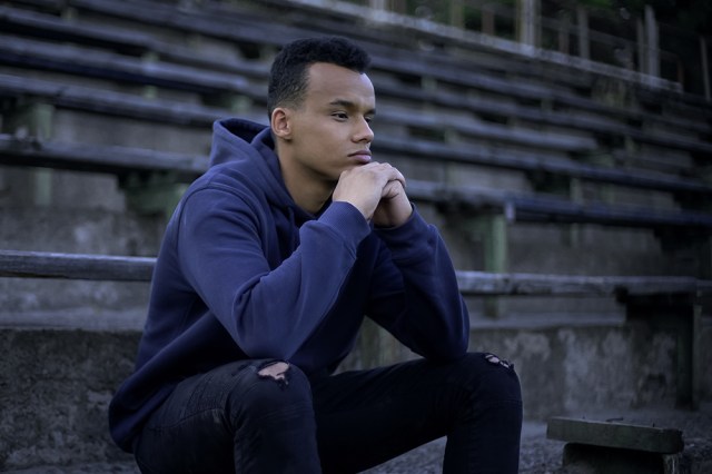 Young man sitting on bleachers in navy hoodie sweatshirt thinking