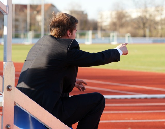 Spectator Trainer Coach sitting in Stadium in Front of Running Track pointing with his hand