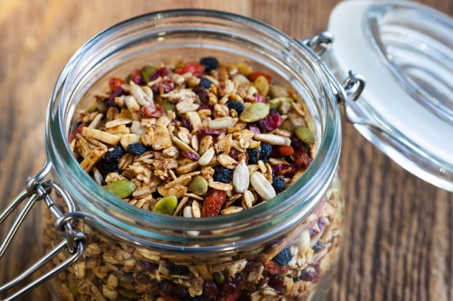 Homemade granola in open glass jar on rustic wooden background