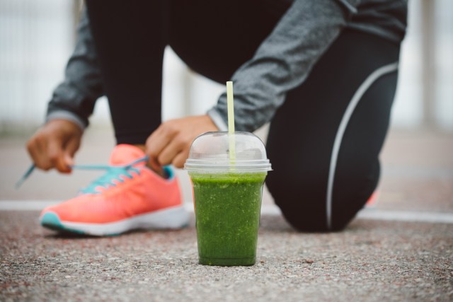 A runner bends down to tie her shoe with a smoothie in front of her foot