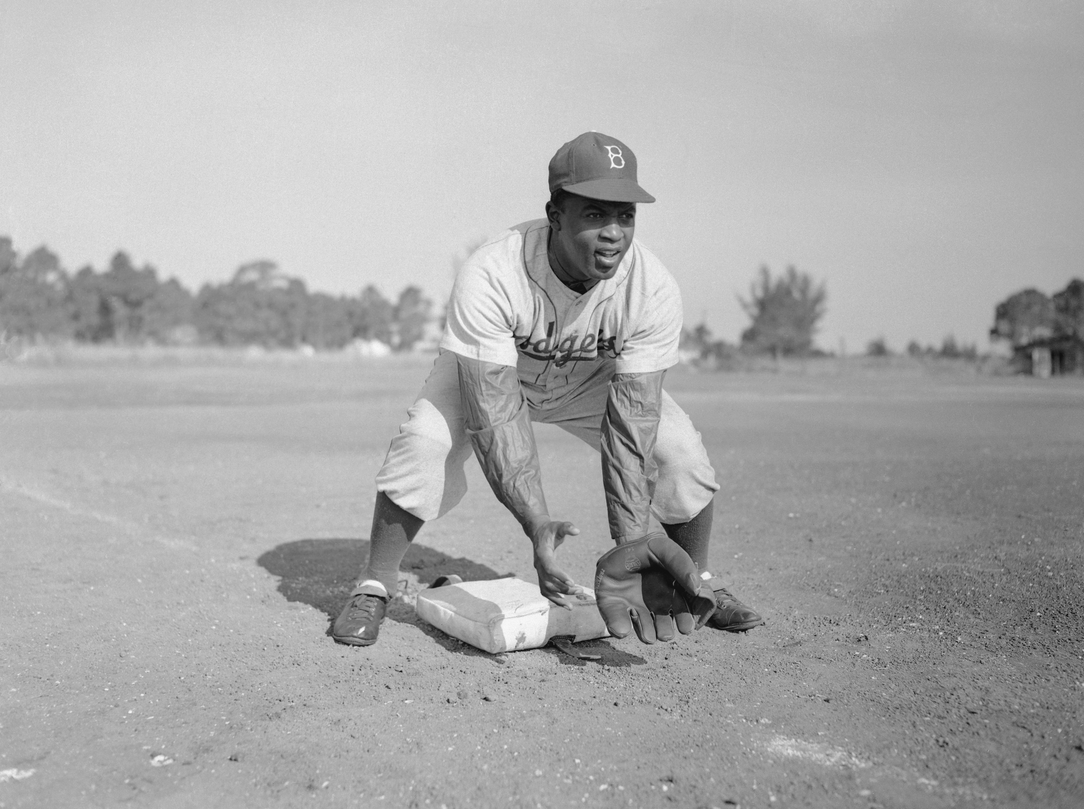 Jackie Robinson during baseball practice bending to catch a ground ball.