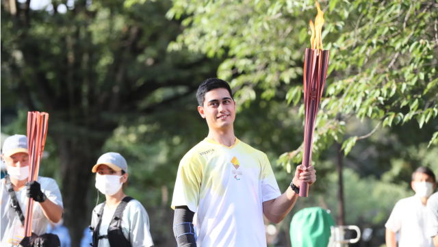 Kai Sakakibara carries Paralympic torch while wearing yellow Paralympic jersey