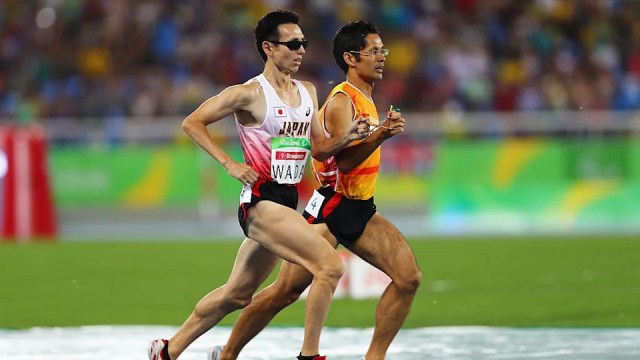 A visually impaired athlete and his guide running in sync during a track event at the Paralympic Games, both in athletic gear with the guide holding a tether.
