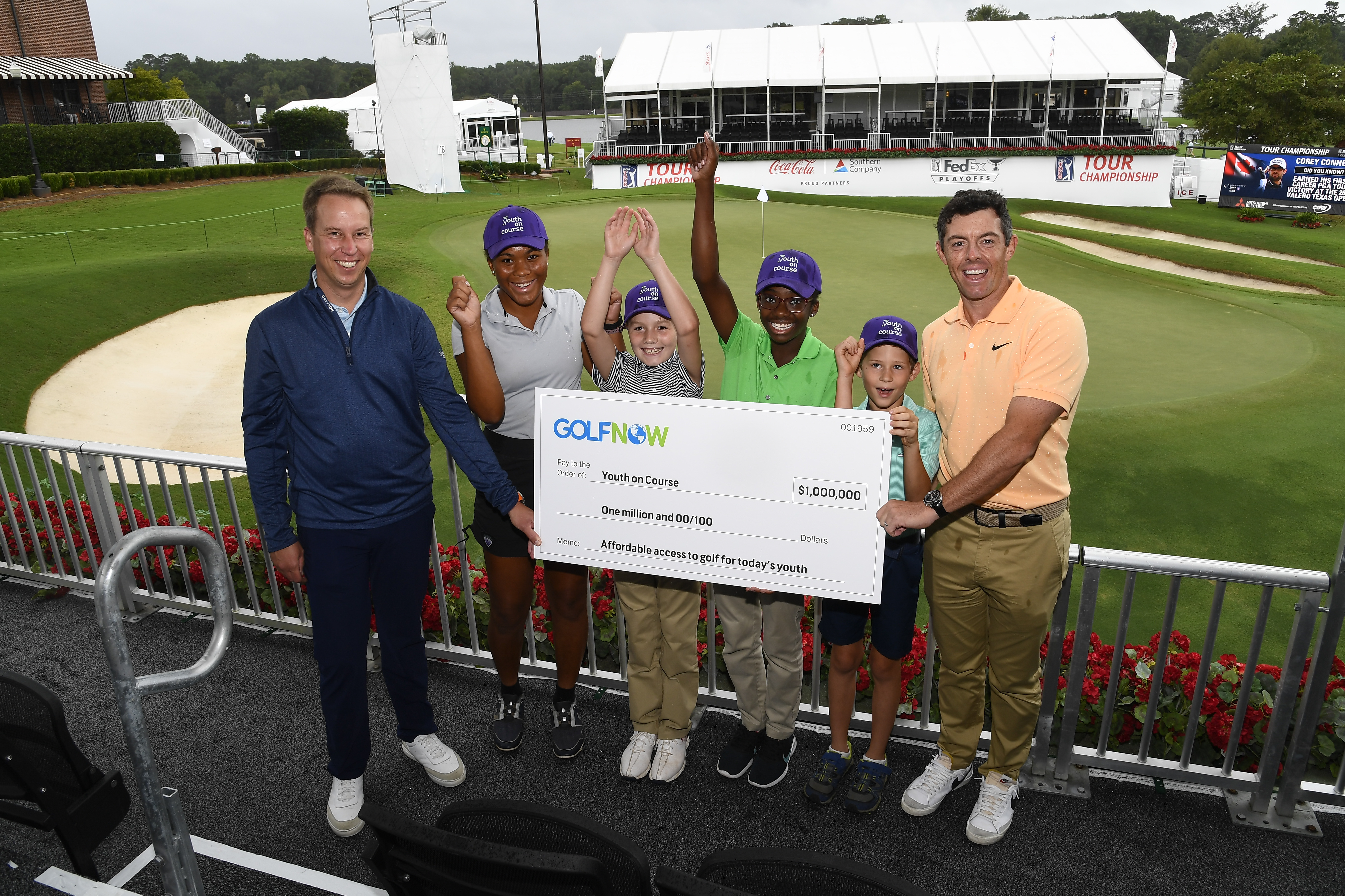 Group photo of YOC CEO Adam Heieck, Rory McIroy, and YOC members on the golf course holding a donation check