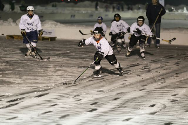 Youth athletes playing hockey at night on a frozen lake at U.S. Pond Hockey Championships