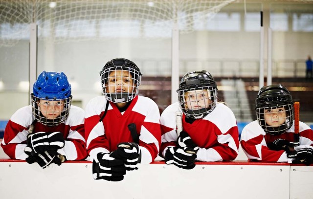 roup of four young ice hockey players leaning on wall of players box in ice hockey arena