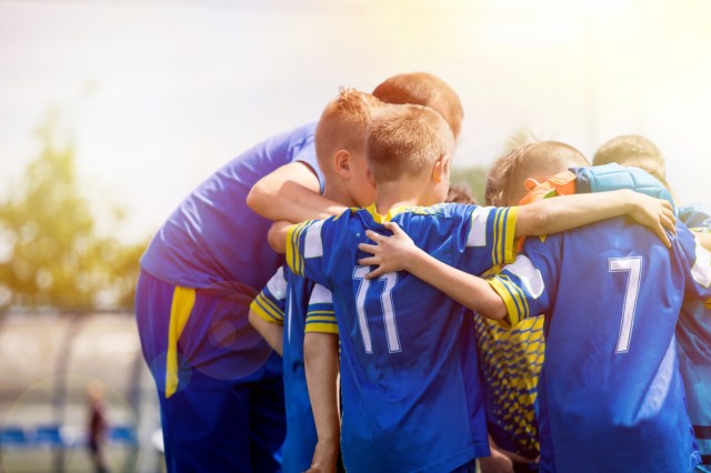 Kids sport team having pep talk with coach. Children soccer team motivated by trainer. Coaching football youth team. Young boys standing together united