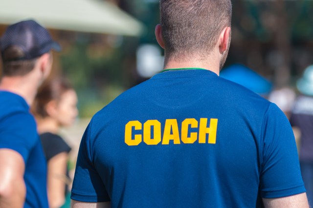 back of a coach's blue color shirt with the word Coach in yellow color written on, blurred background, good for sport or training theme