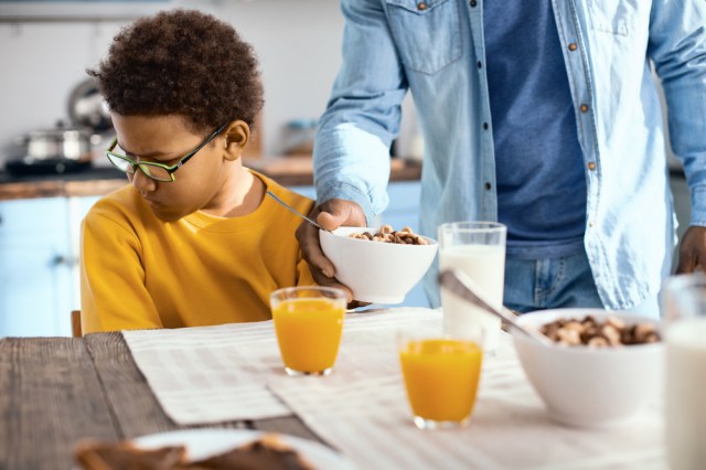 Cute pre-teen boy turning his face away from his father giving him a bowl of cereals, expressing his reluctance to eat