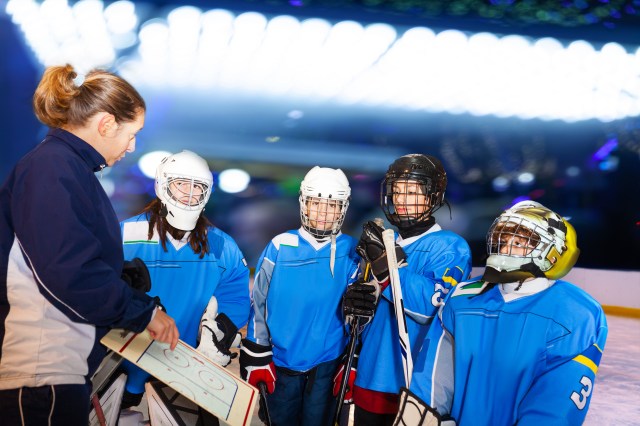 Female coach discussing game plan with young hockey players on ice rink