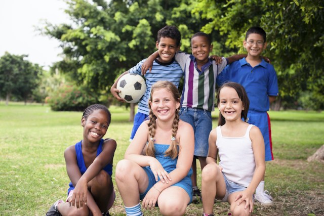 Young boys and sport, portrait of three young children with football looking at camera. Summer camp fun