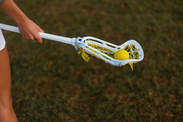 Female lacrosse player holding a women's lacrosse stick on a field.