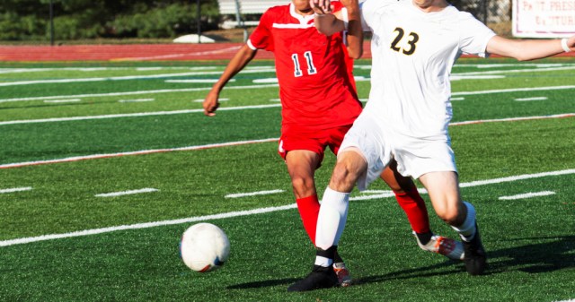 Two high school boys draw contact with each other during a high school soccer game on a green turf field,