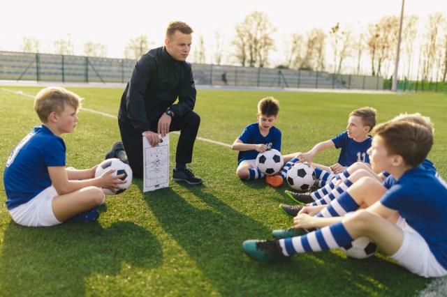 Group of Young Boys Sitting on Sports Grass Field witch School Coach