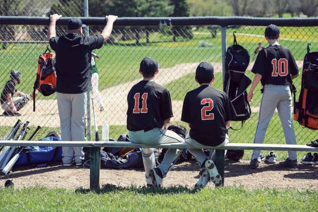 Teenagers in dugout behind chainlink fencing, shallow focus