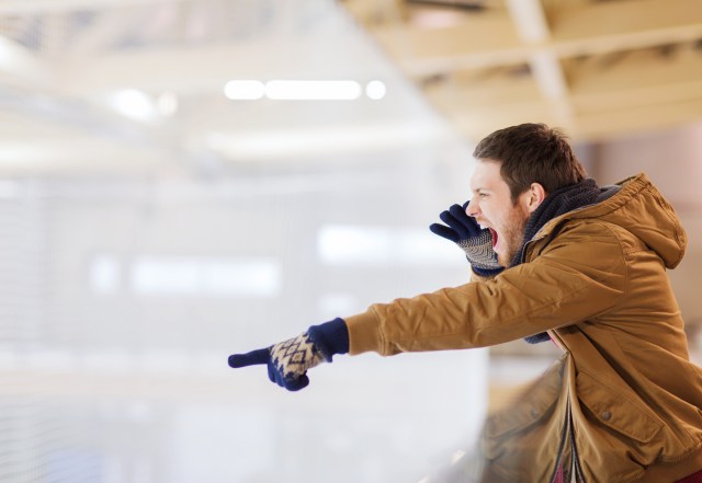 young man supporting hockey game, pointing finger and shouting on skating rink