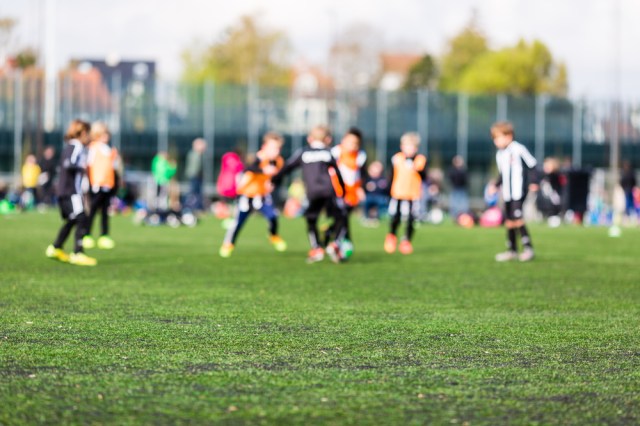 Shallow depth of field shot of young boys playing a kids soccer match on green turf.