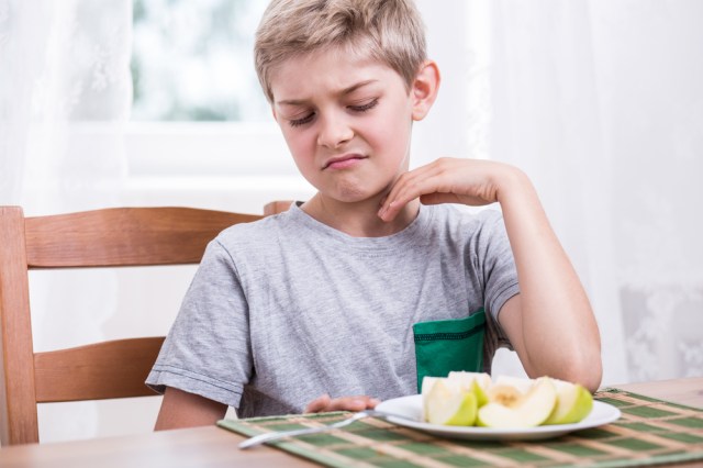 Blonde boy refusing to eat healthy apple