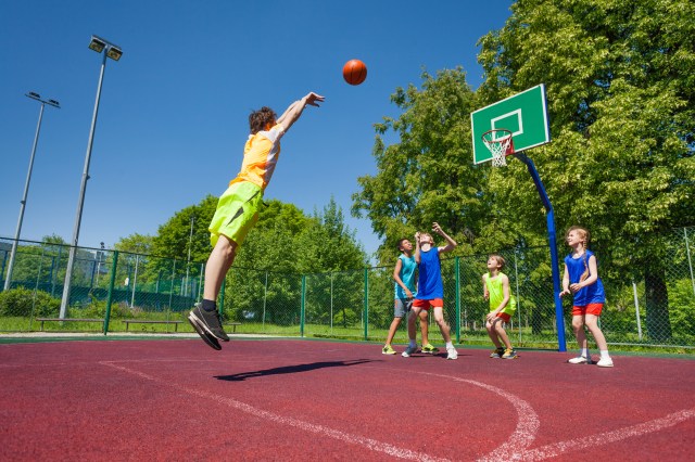Boy performs foul shot at basketball game on the playground during sunny summer day