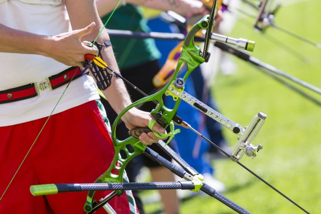 People are shooting with recurve bows during an archery competition. Hands and bows only. Green bow.