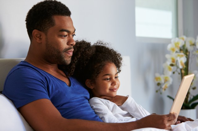Man and daughter sitting in bed watching computer, waist up