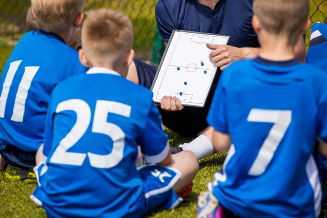 Youth Football Team with Coach at the Soccer Stadium. Boys Listening to Coach's Instructions Before Competition. Coach Giving Team Talk Using Soccer Tactics Board